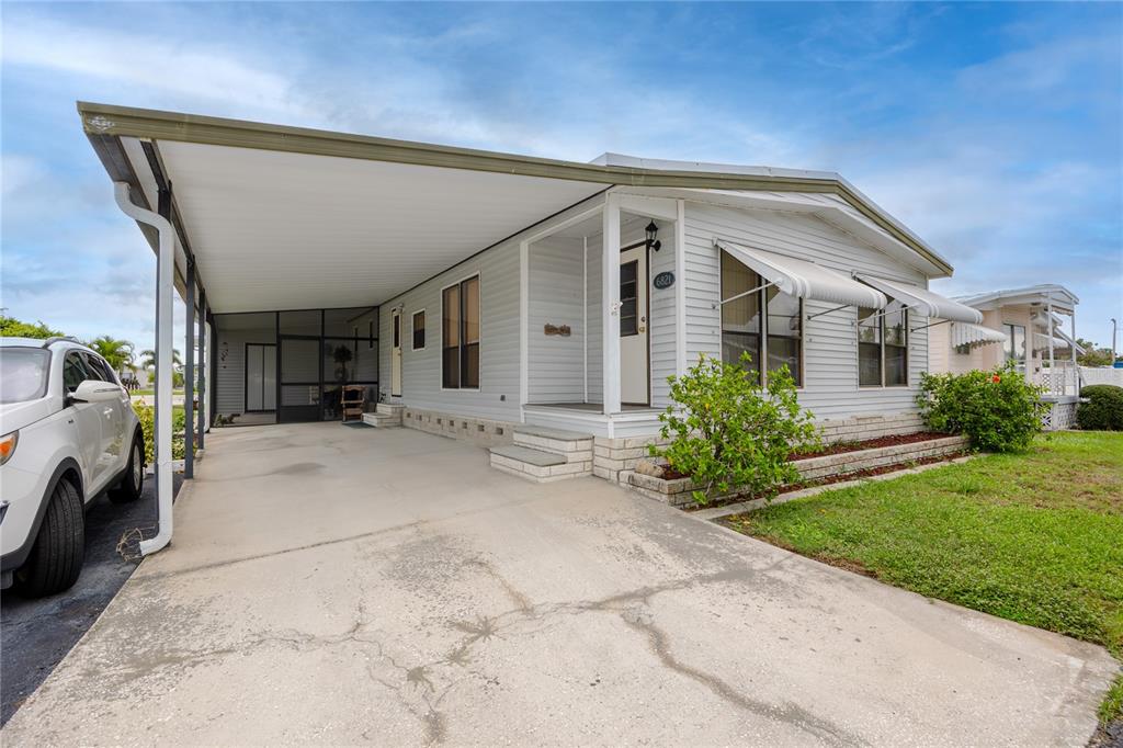 A light gray manufactured home features a large carport, a screened porch, and a concrete driveway — 6821 AMERICANA DRIVE NE UNIT 106, ST PETERSBURG, FL