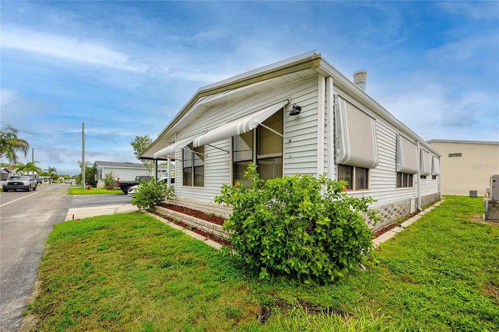 The exterior of a white mobile home features metal window awnings and a small garden — 6821 AMERICANA DRIVE NE UNIT 106, ST PETERSBURG, FL