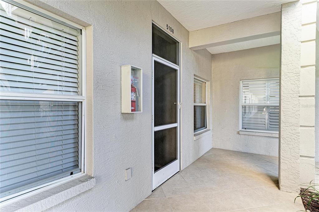 A covered entryway features a tiled floor, a screen door, and a wall-mounted fire extinguisher — 9620 CLUB SOUTH CIRCLE UNIT 5108, SARASOTA, FL