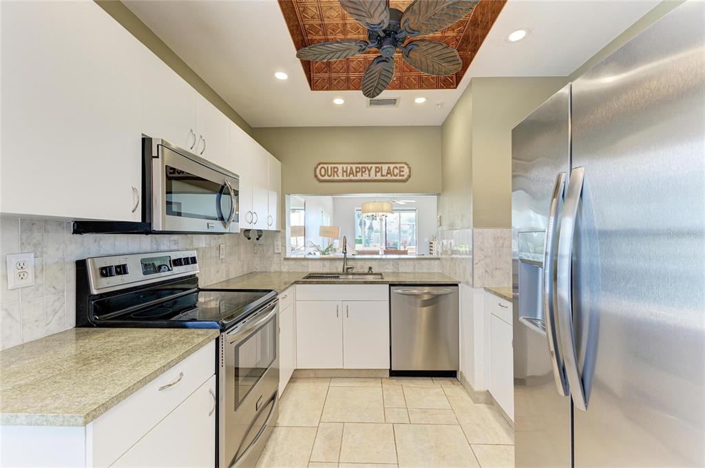 A kitchen features white cabinets, stainless steel appliances, a tiled backsplash, and a decorative ceiling — 9620 CLUB SOUTH CIRCLE UNIT 5108, SARASOTA, FL