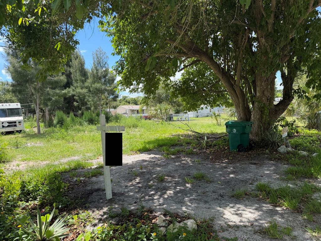 A vacant, grassy lot features a real estate sign and a large tree with a bin — 5497 MAZE DRIVE, PUNTA GORDA, FL