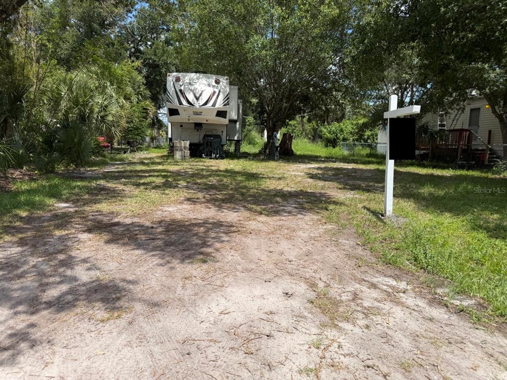 A large RV is parked on a dirt lot with trees and a real estate sign — 5497 MAZE DRIVE, PUNTA GORDA, FL