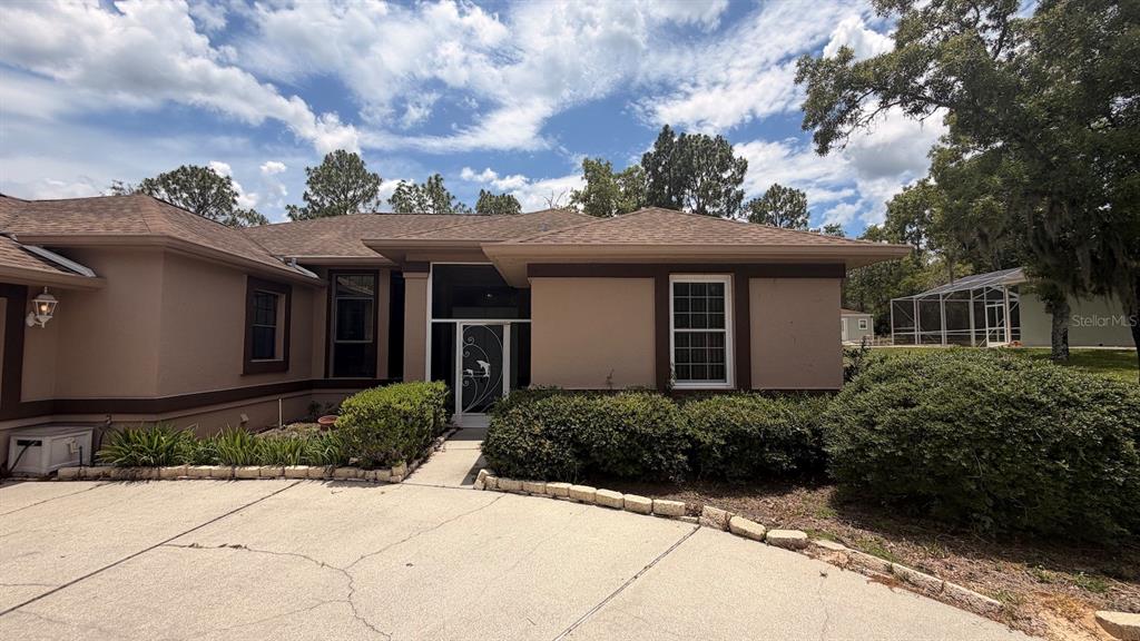 The exterior of a tan house features a screened entryway, brown trim, and a driveway — 2496 E NEWHAVEN STREET, INVERNESS, FL