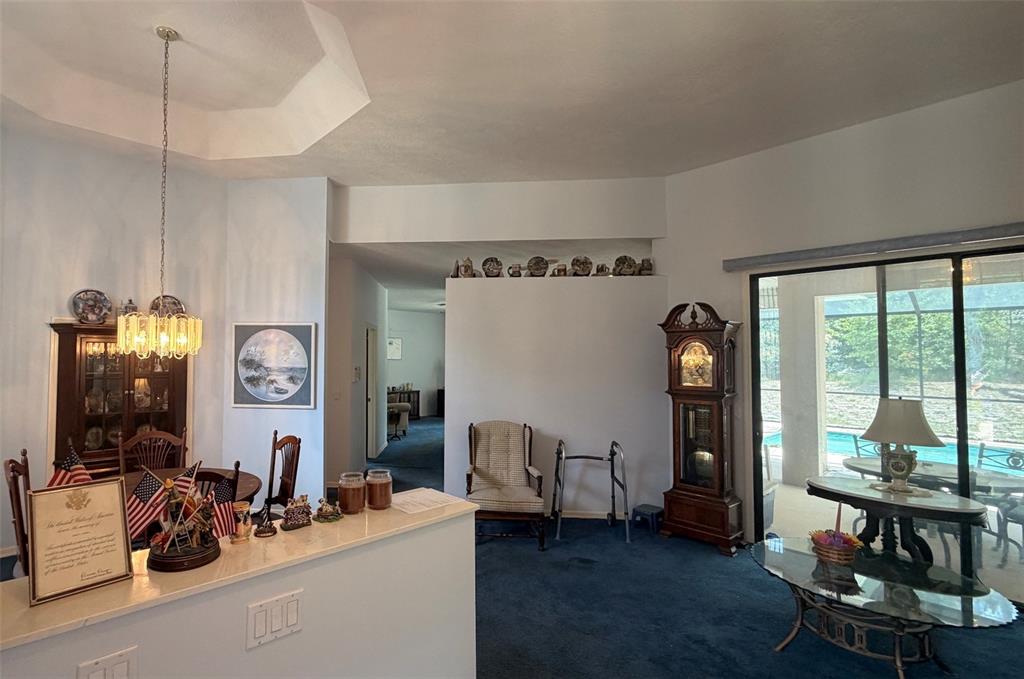 A dining area and living space feature blue carpeting, a grandfather clock, and sliding glass doors — 2496 E NEWHAVEN STREET, INVERNESS, FL