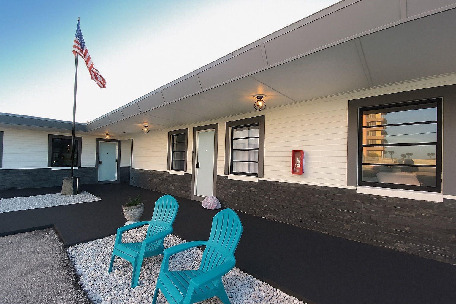 Exterior view of a motel building with white siding, dark stone accents, and turquoise chairs — 1915 N Atlantic Avenue, FL 32118, FL