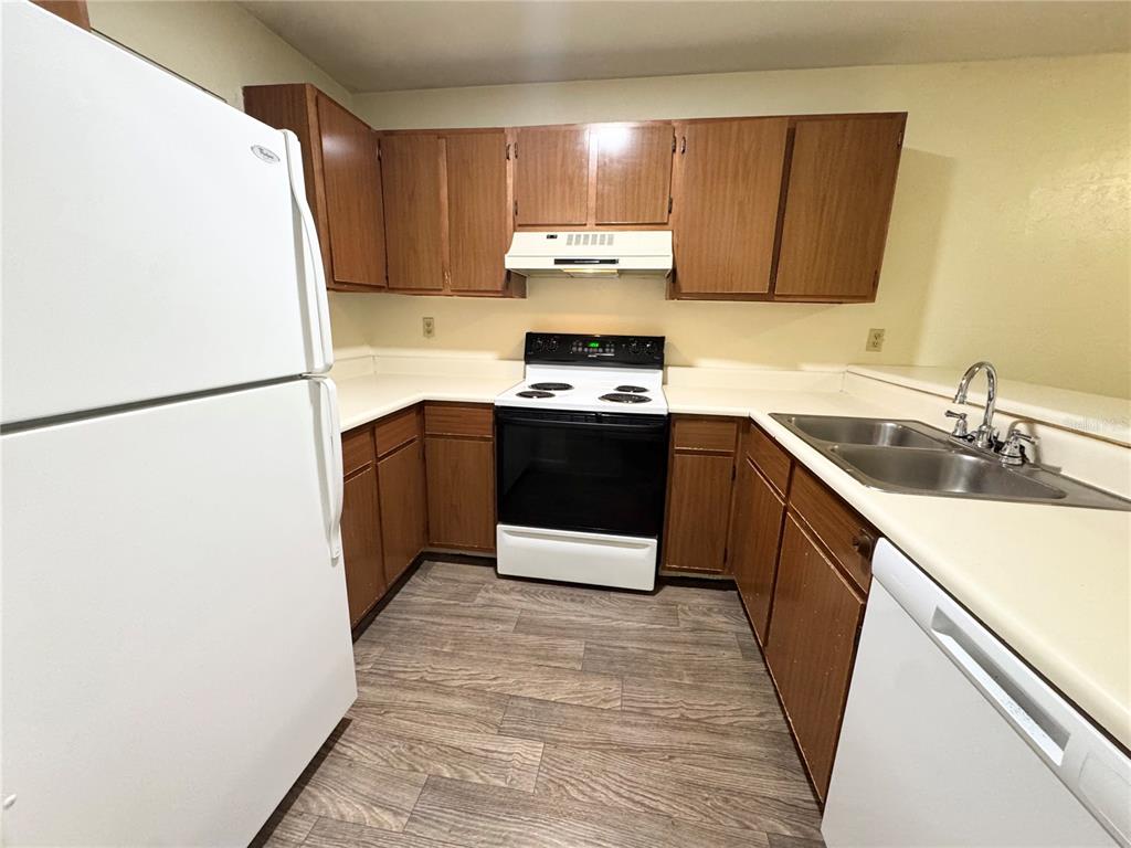 A kitchen features wood cabinets, white appliances, a double sink, and light-colored countertops — 83 SE 16TH AVENUE UNIT E303, GAINESVILLE, FL