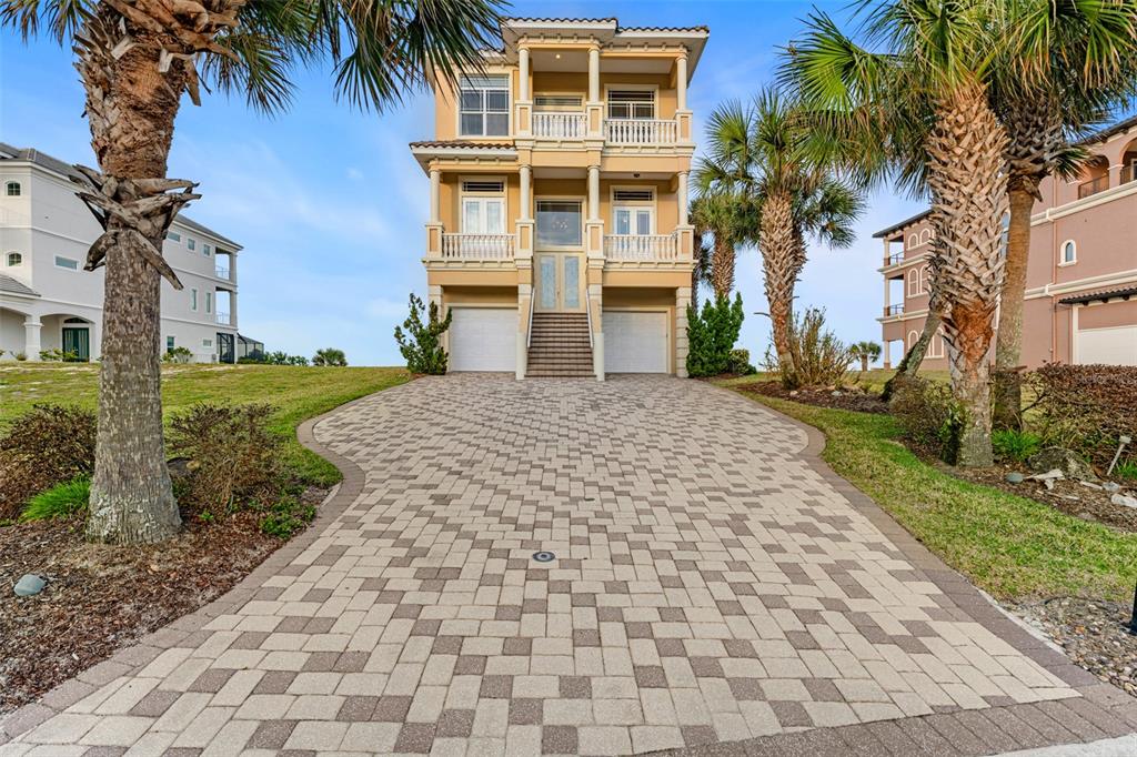 A three-story tan house with a paved driveway and palm trees in the front yard — 6 HAMMOCK BEACH COURT, PALM COAST, FL