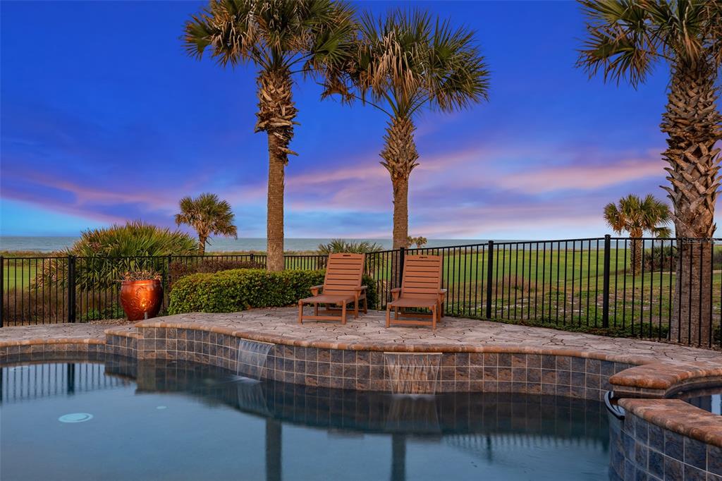 A swimming pool with water features sits before two lounge chairs and a fenced yard — 6 HAMMOCK BEACH COURT, PALM COAST, FL