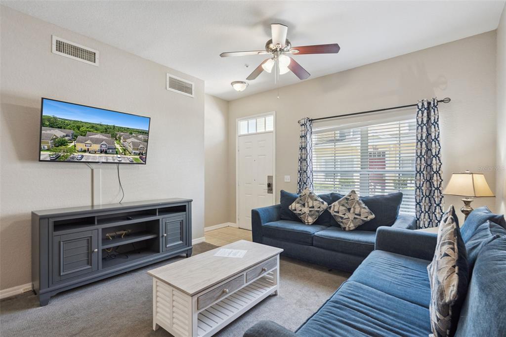 A living room features a blue sofa, a television, a coffee table, and a ceiling fan — 4560 YELLOWGOLD ROAD E UNIT 103, KISSIMMEE, FL