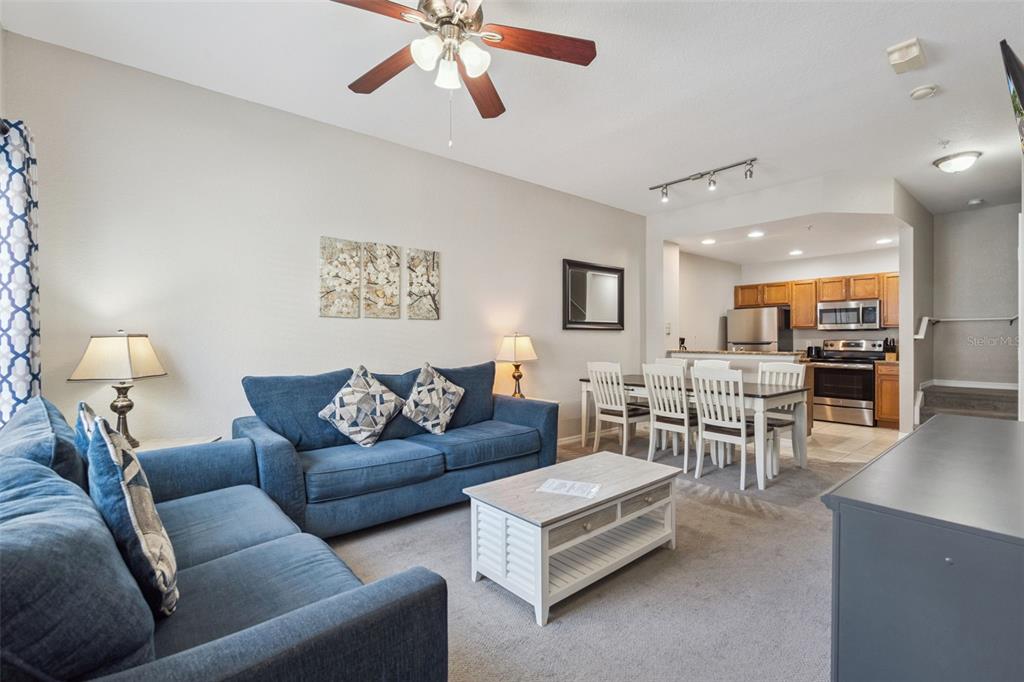 A living room with blue sofas and a coffee table opens to a dining area — 4560 YELLOWGOLD ROAD E UNIT 103, KISSIMMEE, FL