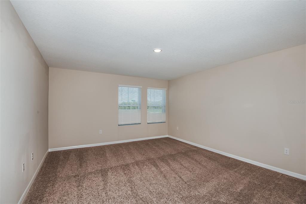 An empty bedroom features beige walls, brown carpeting, and two windows with white blinds — 6028 PRAIRIE RUN, HAINES CITY, FL