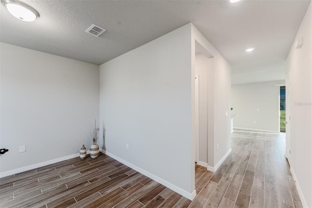 An interior view shows a room with wood-look tile flooring and a hallway leading outside — 5252 SANDERS OAK TRAIL, ST CLOUD, FL