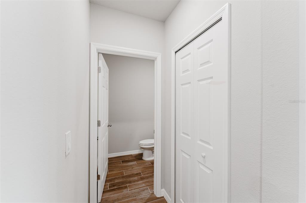 A hallway with wood-look tile flooring leads to a bathroom with a toilet — 5252 SANDERS OAK TRAIL, ST CLOUD, FL