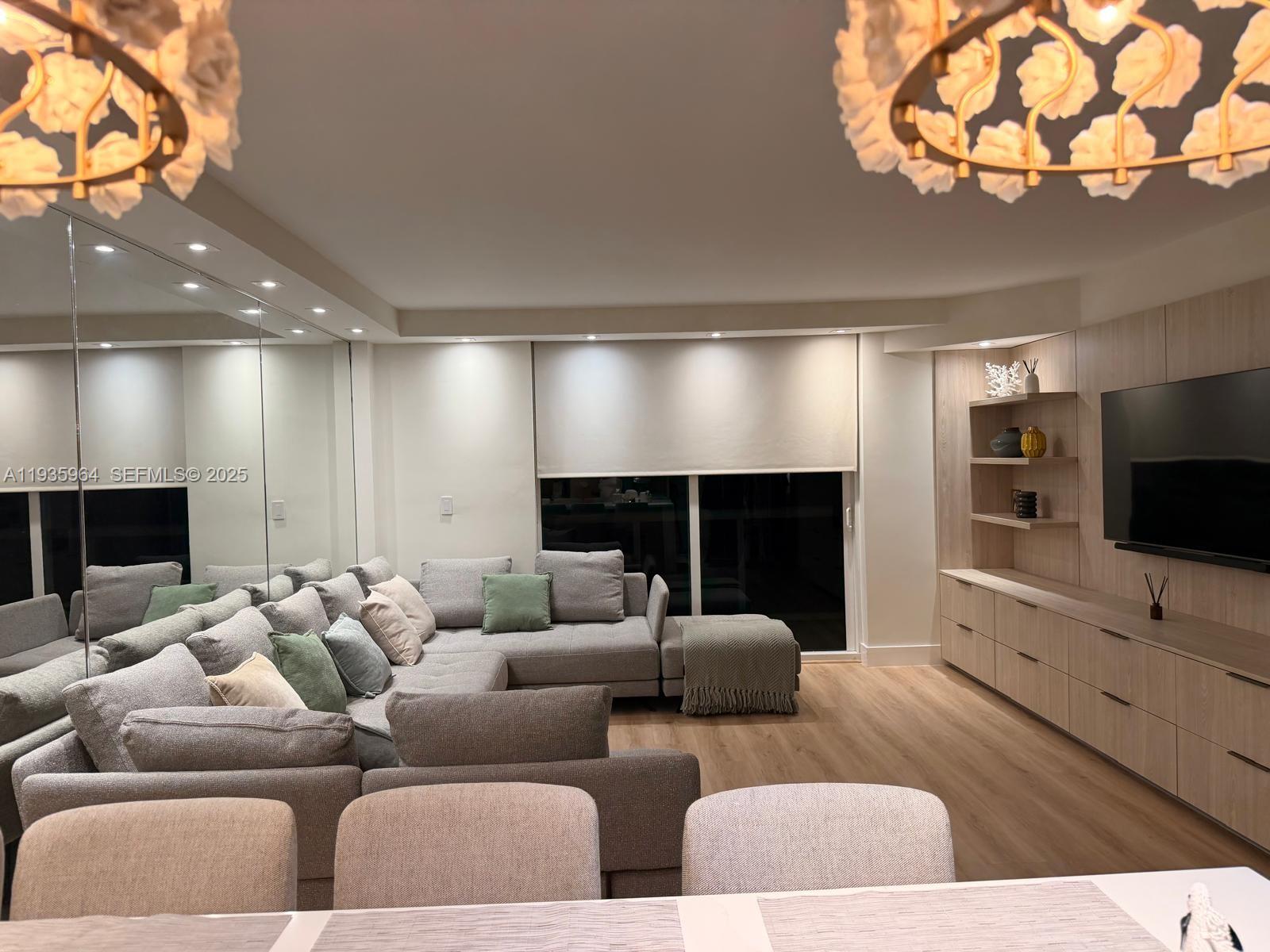 A modern living room features a large gray sectional sofa, built-in cabinetry, and mirrored walls — 10275 Collins Ave # 333, Bal Harbour FL 33154, BAL HARBOUR, FL