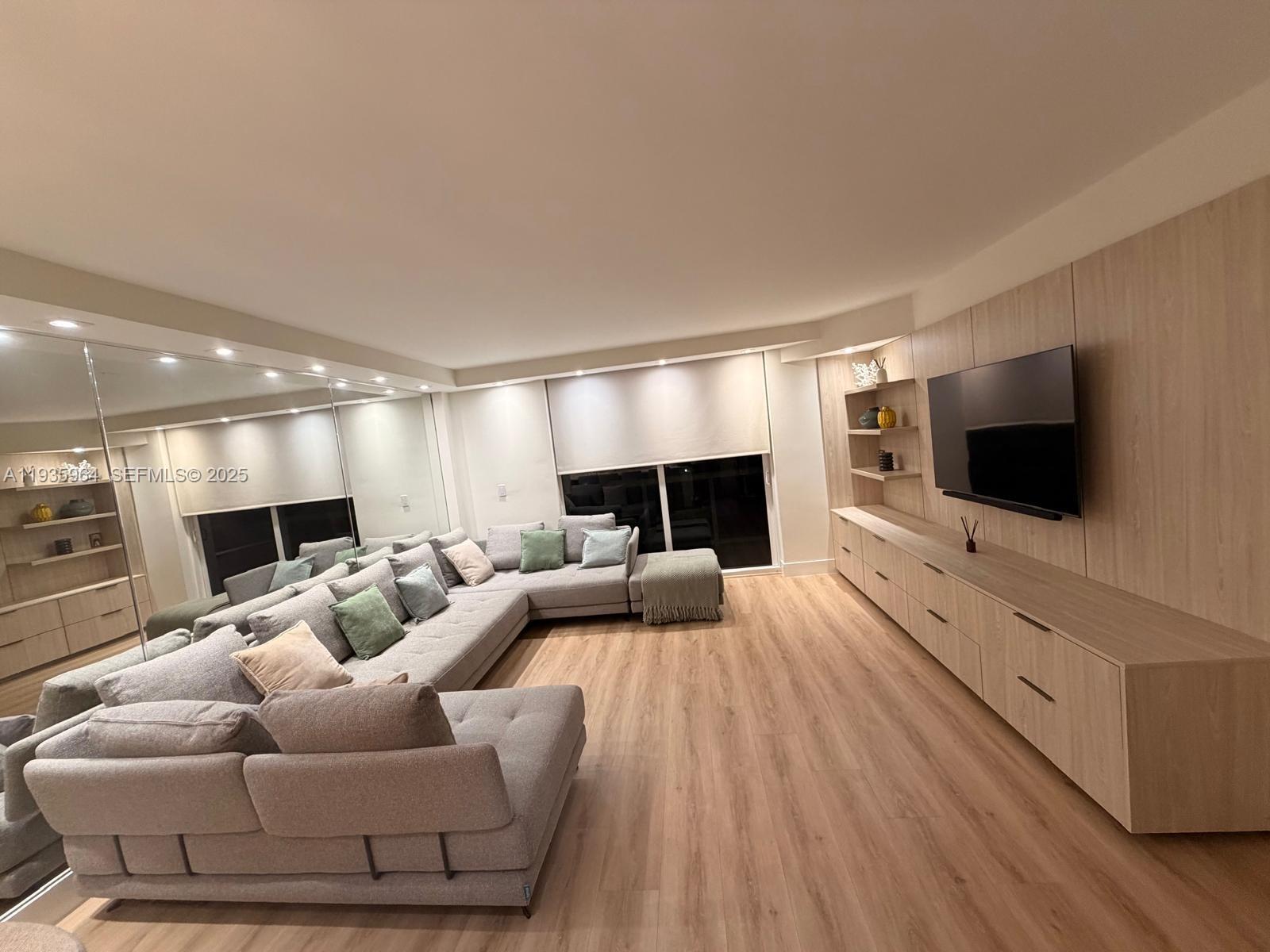 A living room features a large gray sectional sofa, light wood cabinetry, and a mirrored wall — 10275 Collins Ave # 333, Bal Harbour FL 33154, BAL HARBOUR, FL