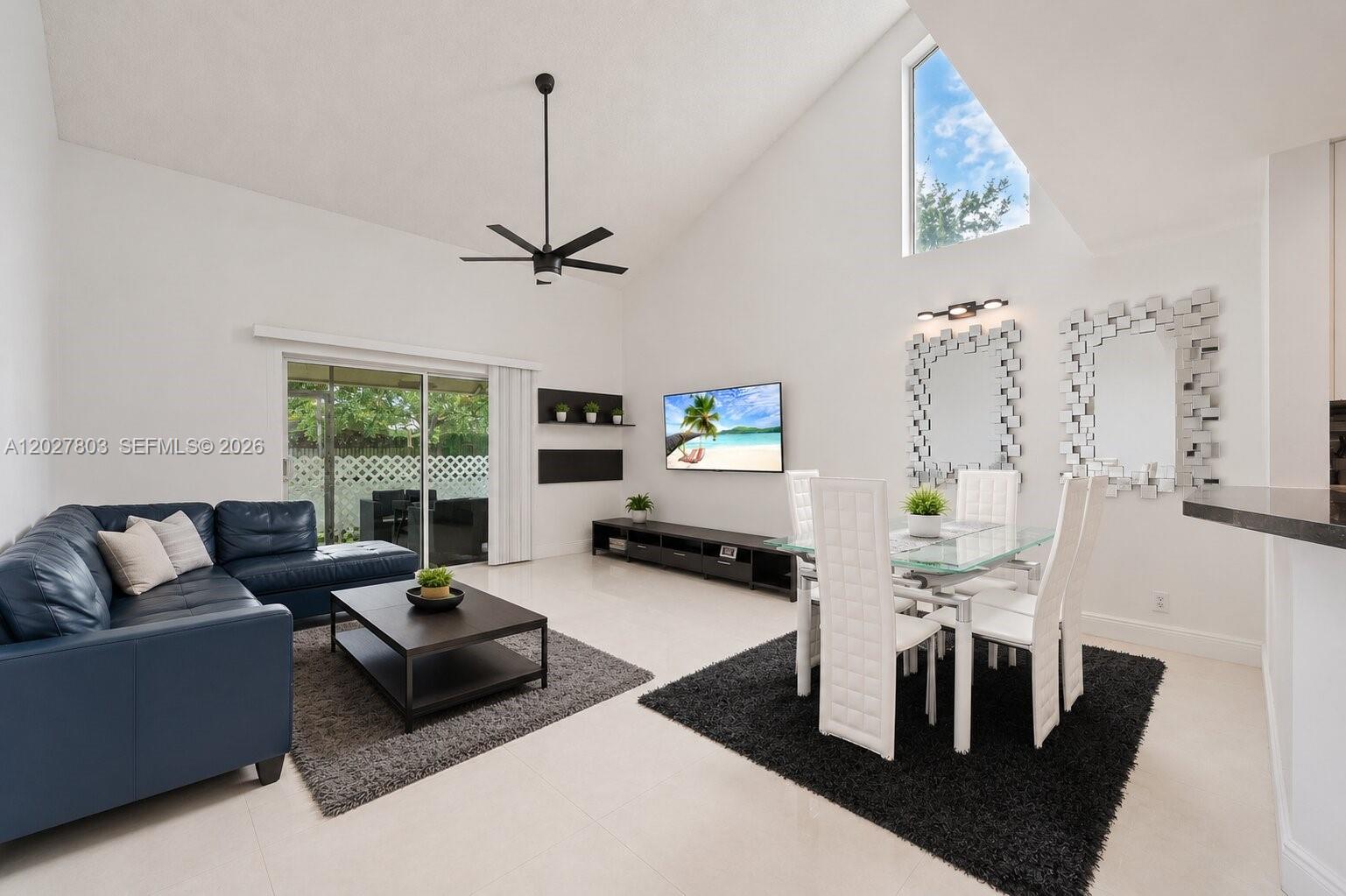 A living and dining area features a vaulted ceiling, blue sofa, and glass-topped table — 15723 Woodgate Pl, Sunrise FL 33326, SUNRISE, FL