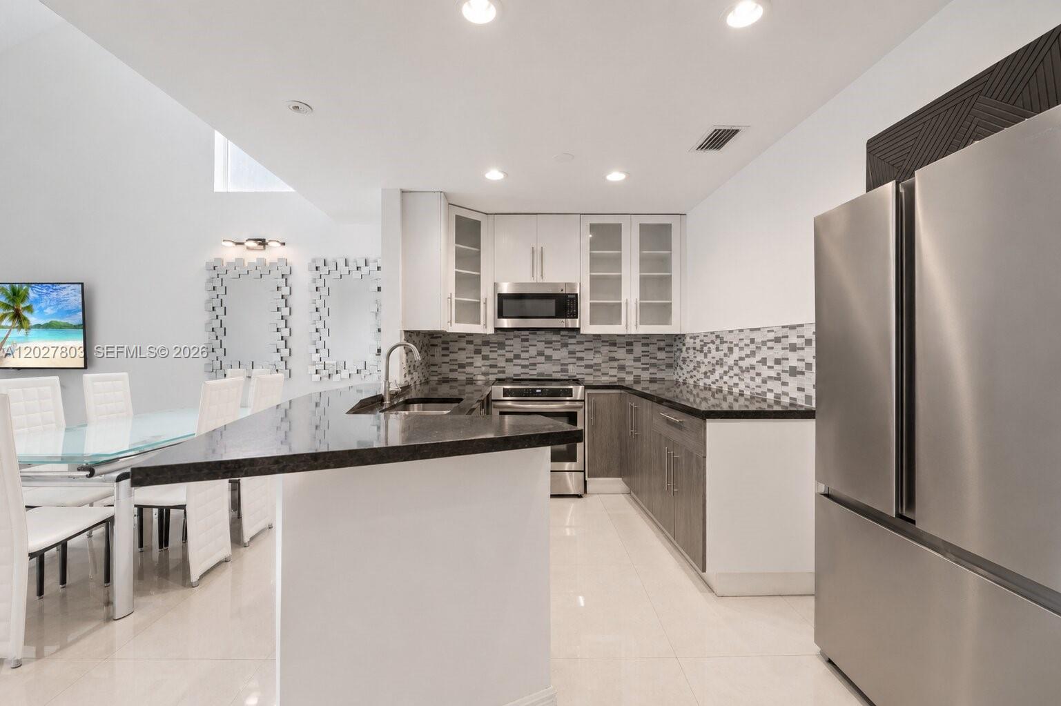 A modern kitchen features dark countertops, grey cabinetry, stainless steel appliances, and a breakfast bar — 15723 Woodgate Pl, Sunrise FL 33326, SUNRISE, FL