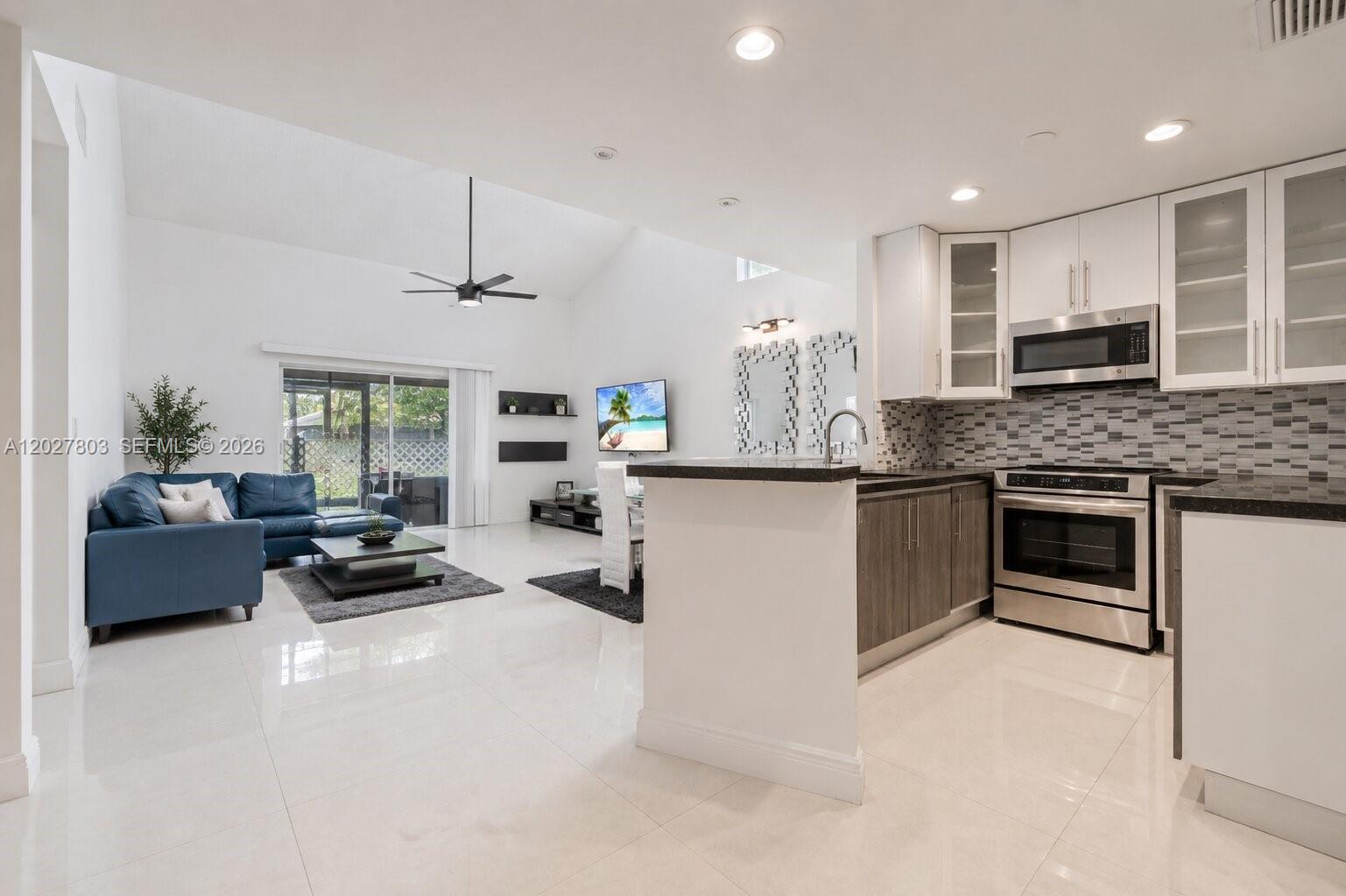 A modern kitchen with dark cabinets and stainless appliances opens into a bright living area — 15723 Woodgate Pl, Sunrise FL 33326, SUNRISE, FL