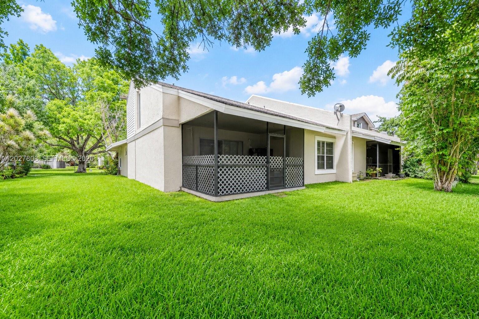 The exterior of a single-story home features a screened-in patio and a large grassy yard — 15723 Woodgate Pl, Sunrise FL 33326, SUNRISE, FL