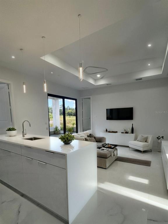 A modern open-concept kitchen and living area features white cabinetry, marble-look flooring, and recessed lighting — 409 WESTERN AVENUE S, LEHIGH ACRES, FL