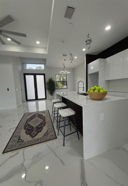 A modern kitchen features a white quartz waterfall island, bar stools, and marble-look tile flooring — 409 WESTERN AVENUE S, LEHIGH ACRES, FL