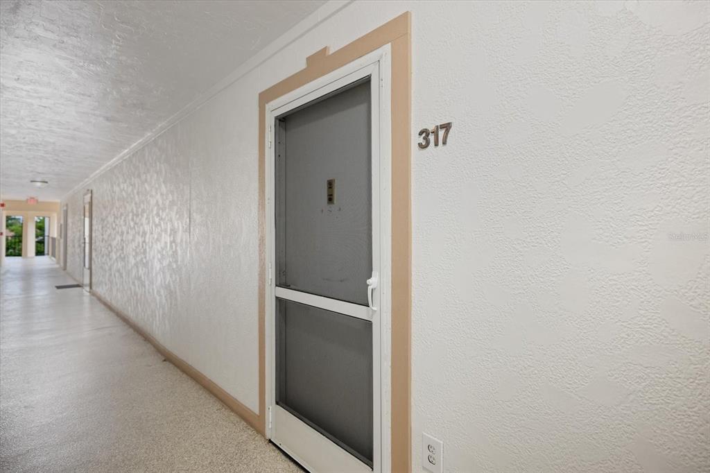 A hallway in an apartment complex features a screen door labeled 317 — 618 BIRD BAY DRIVE S UNIT 317, VENICE, FL