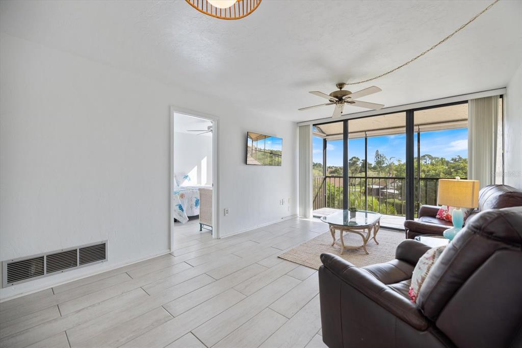 A living room with light tile floors, a ceiling fan, and a balcony with views — 618 BIRD BAY DRIVE S UNIT 317, VENICE, FL