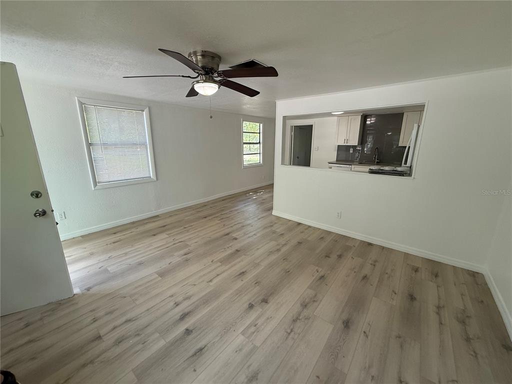 A living room with light wood-look flooring, a ceiling fan, and a kitchen pass-through window — 3424 MAZE LANE, BRANDON, FL
