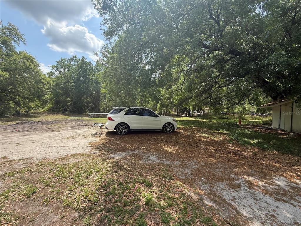A white SUV is parked on a dirt lot under large oak trees — 3424 MAZE LANE, BRANDON, FL