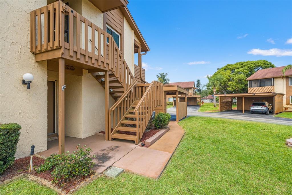 An exterior view of a two-story apartment building with wooden stairs and a covered carport — 3836 LIGHTHOUSE WAY UNIT 3836, NEW PORT RICHEY, FL
