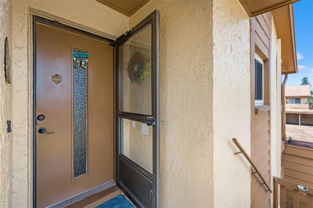 A brown front door with a glass insert and a screen door on a balcony — 3836 LIGHTHOUSE WAY UNIT 3836, NEW PORT RICHEY, FL