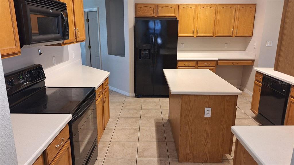 A kitchen features oak cabinets, white countertops, a center island, and black appliances — 1803 LAKE VILLA DRIVE, TAVARES, FL