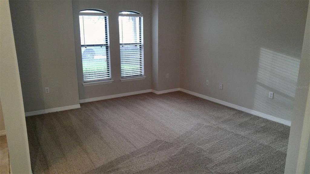 An empty bedroom features gray carpet, light gray walls, and two arched windows with blinds — 1803 LAKE VILLA DRIVE, TAVARES, FL