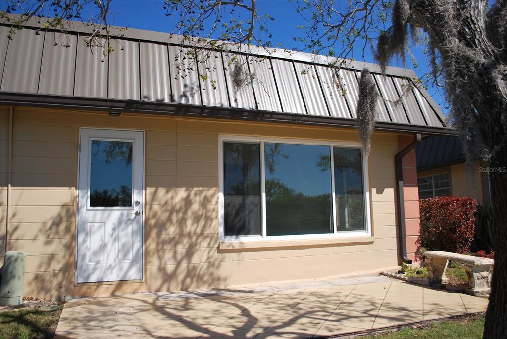 A tan exterior wall with a white door, large window, and a tiled patio area — 4136 STRATFORD DRIVE, NEW PORT RICHEY, FL