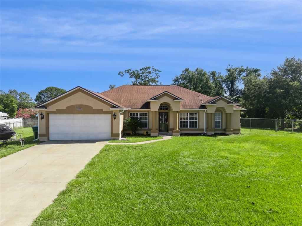 A single-story house with a tan stucco exterior, a two-car garage, and a front lawn — 1560 GRAY COURT, DELTONA, FL