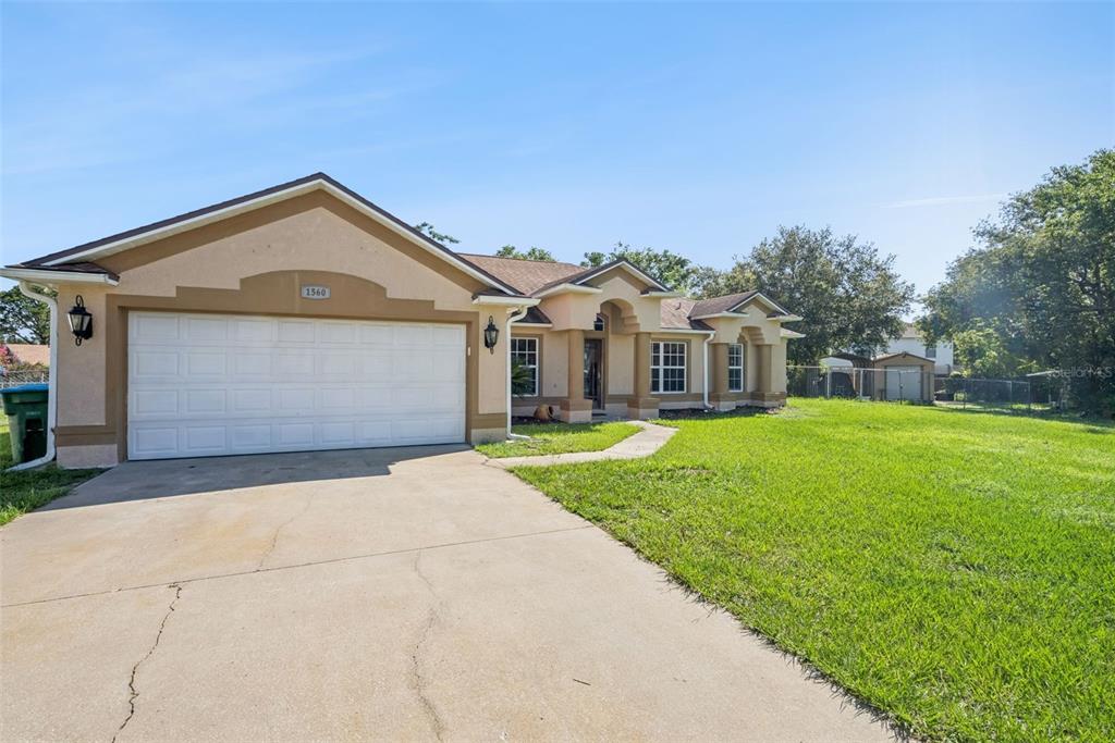 A single-story house with a beige stucco exterior, a two-car garage, and a concrete driveway — 1560 GRAY COURT, DELTONA, FL