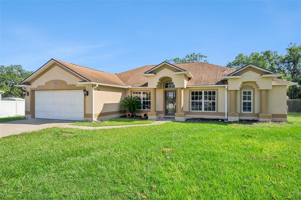 A single-story tan stucco house with a two-car garage and a front lawn — 1560 GRAY COURT, DELTONA, FL