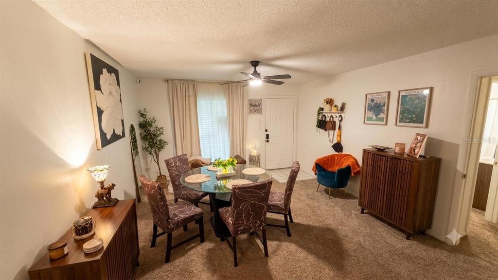 A dining area features a glass-top table, patterned chairs, a ceiling fan, and carpeted flooring — 1711 GROVE STREET UNIT 519, MAITLAND, FL