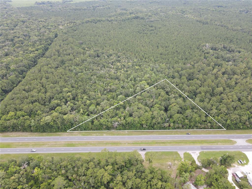 An aerial view shows a triangular plot of wooded land bordering a multi-lane highway — TBD SE HIGHWAY 19, INGLIS, FL
