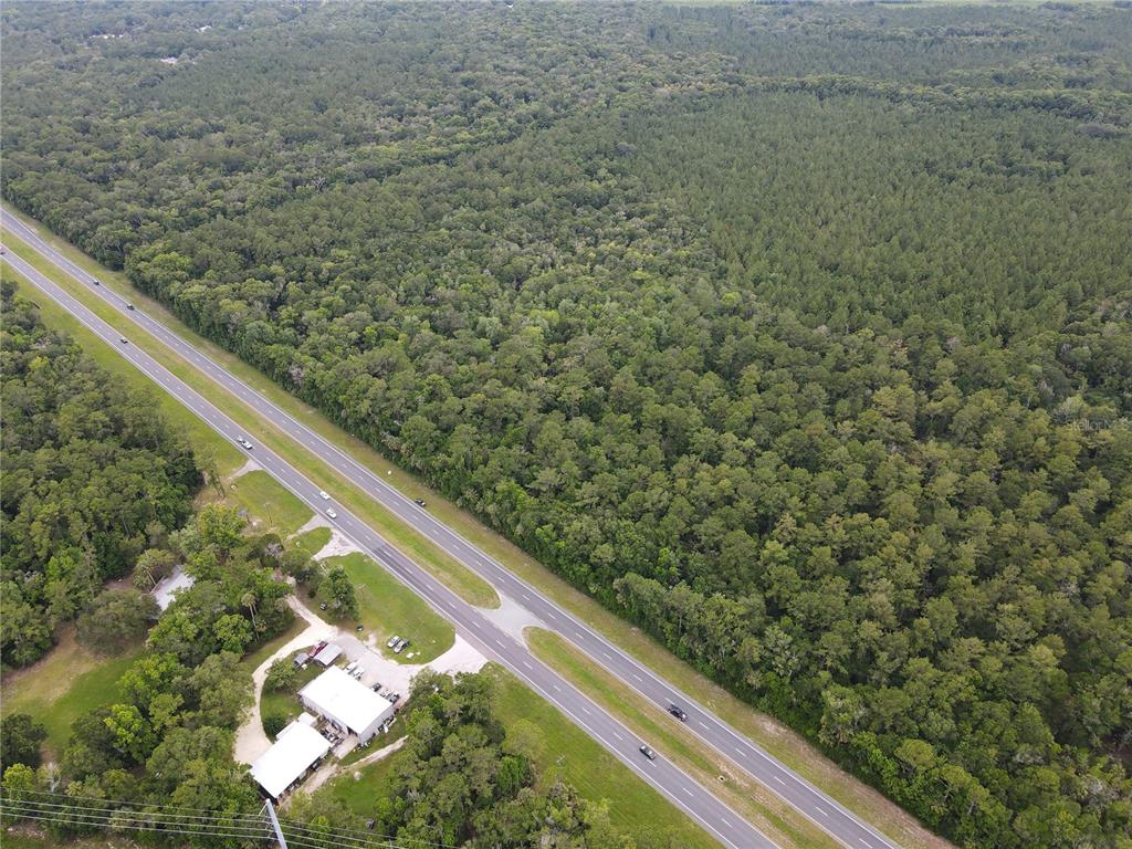 An aerial view shows a highway running past a wooded area and a small building — TBD SE HIGHWAY 19, INGLIS, FL