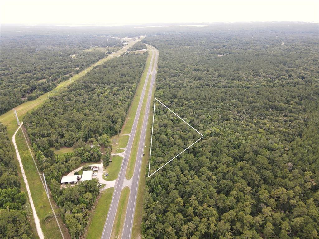 An aerial view shows a triangular plot of land adjacent to a divided highway — TBD SE HIGHWAY 19, INGLIS, FL