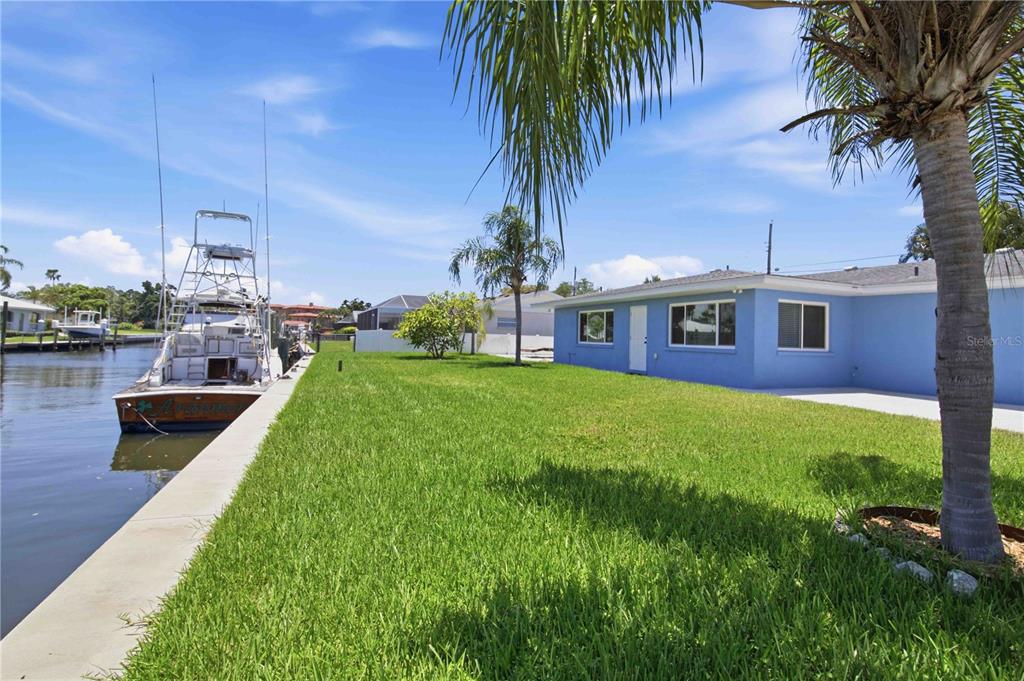 A blue house sits next to a canal with a boat docked along the seawall — 908 24TH AVENUE W, PALMETTO, FL