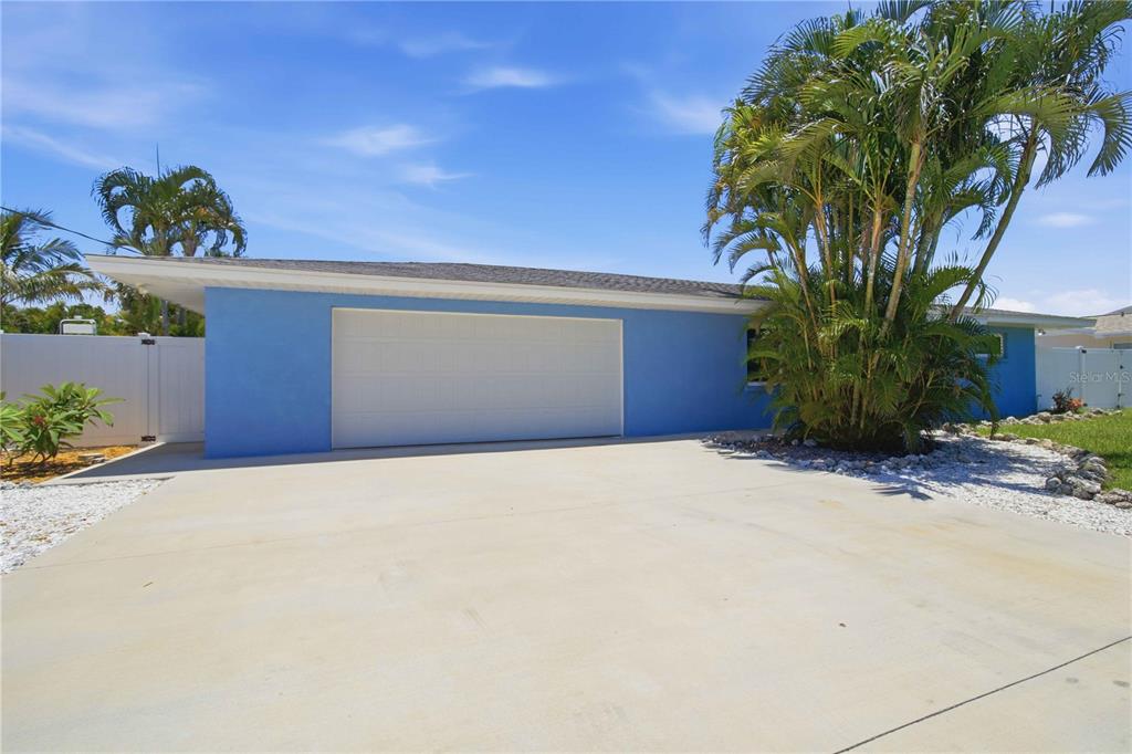 A blue house exterior features a white garage door, a concrete driveway, and palm trees — 908 24TH AVENUE W, PALMETTO, FL
