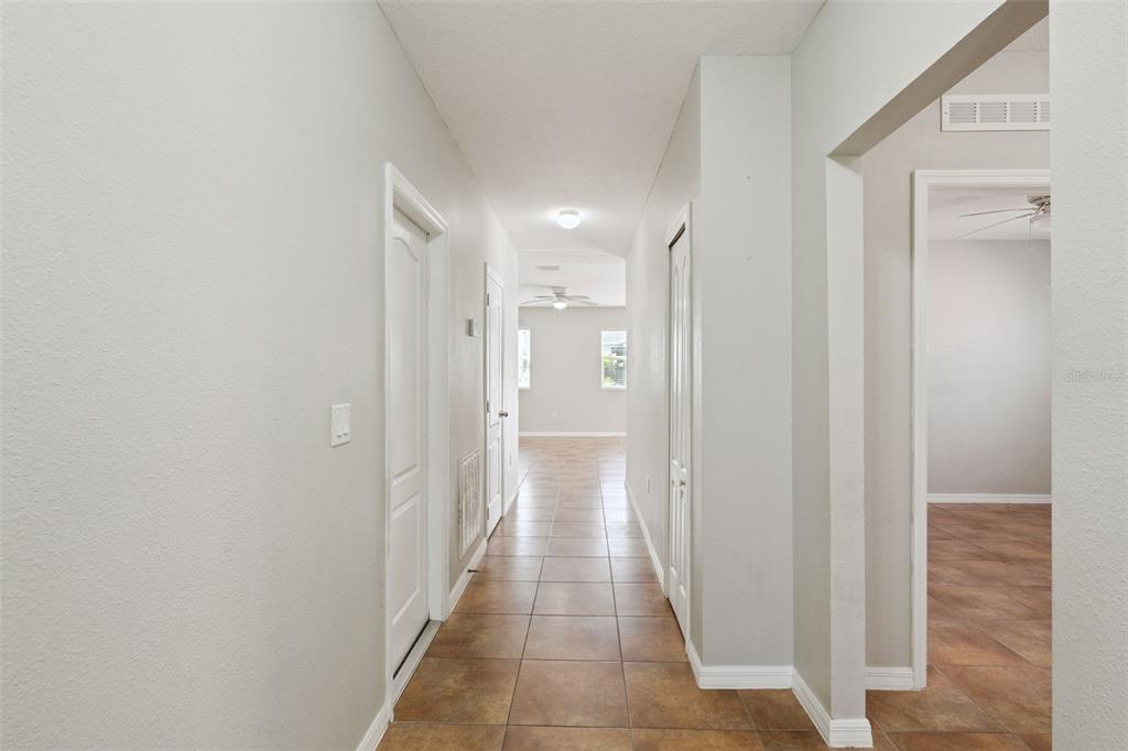 A hallway with light gray walls and brown tile flooring leads to an open room — 1038 SUFFRAGETTE CIRCLE, HAINES CITY, FL