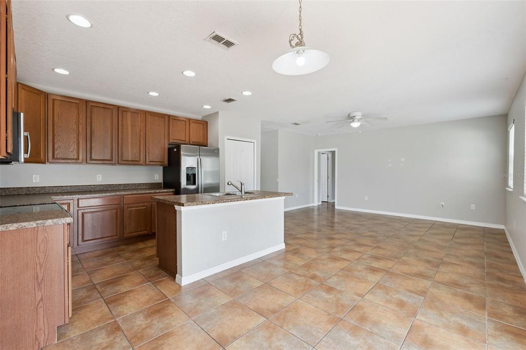 A kitchen with wood cabinets and a granite island opens into a large tiled room — 1038 SUFFRAGETTE CIRCLE, HAINES CITY, FL