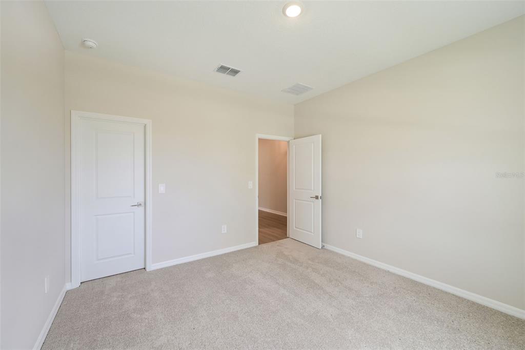 An empty bedroom features beige walls, light-colored carpeting, and two white interior doors — 5924 FRESH FLORA DRIVE, WIMAUMA, FL