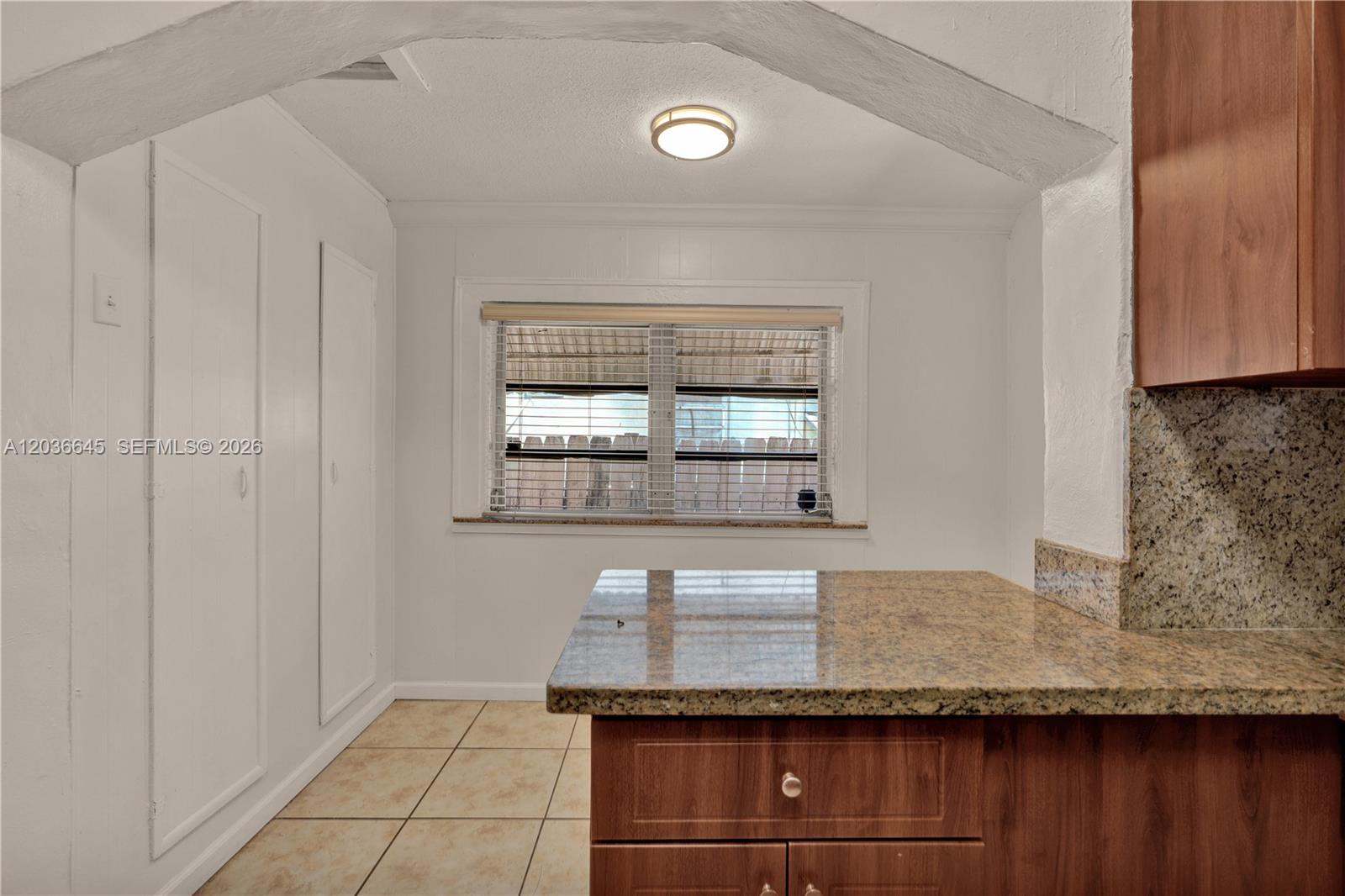 A kitchen area features a granite countertop, wooden cabinets, tile flooring, and a window — 2145 SW 7th St # 1, Miami FL 33135, MIAMI, FL