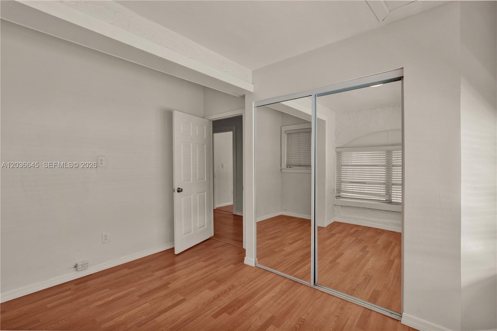 A bedroom features light gray walls, wood-look flooring, a white door, and mirrored closet doors — 2145 SW 7th St # 1, Miami FL 33135, MIAMI, FL