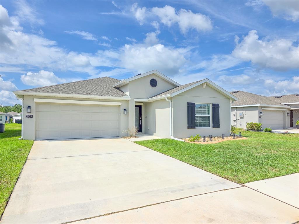 A single-story house with a beige stucco exterior, a two-car garage, and a concrete driveway — 207 WINGED FOOT LANE, DAYTONA BEACH, FL