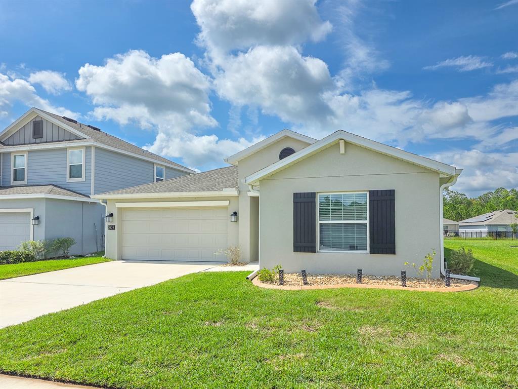 A single-story house with a beige stucco exterior, a two-car garage, and black shutters — 207 WINGED FOOT LANE, DAYTONA BEACH, FL